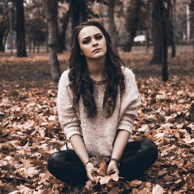 A woman sits outside on leaves in the the fall
