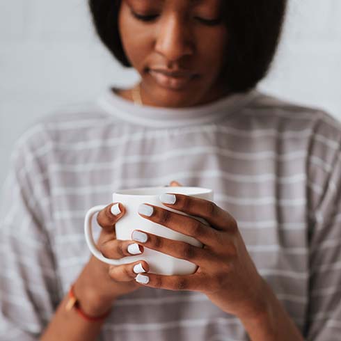 A young woman holds a mug an looks down thoughtfully
