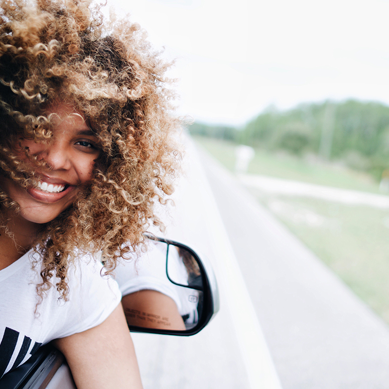 a Black woman smiling out of the passenger window of a car