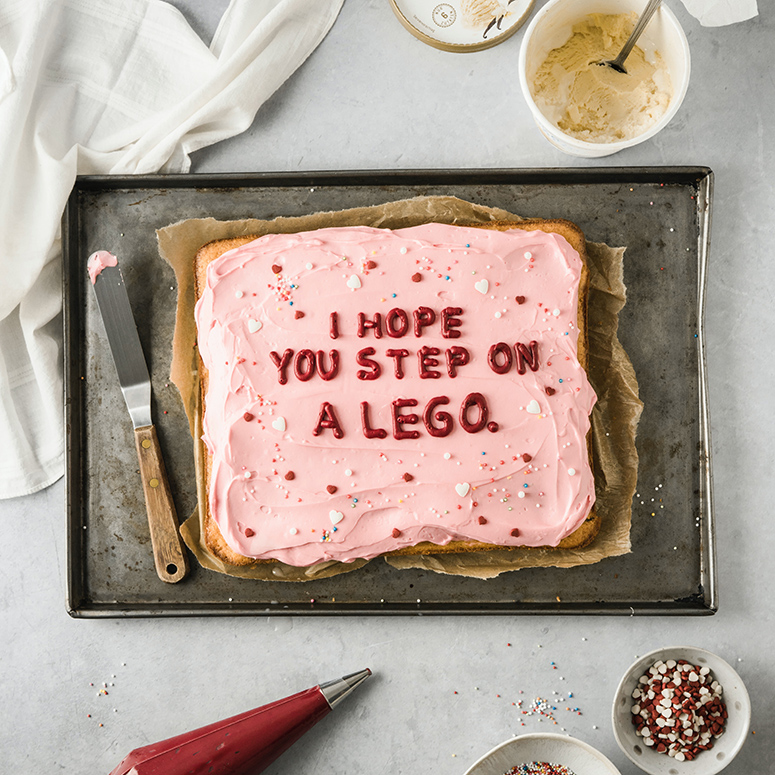 A cake with frosting, and the words 'I hope you step on a lego' written out