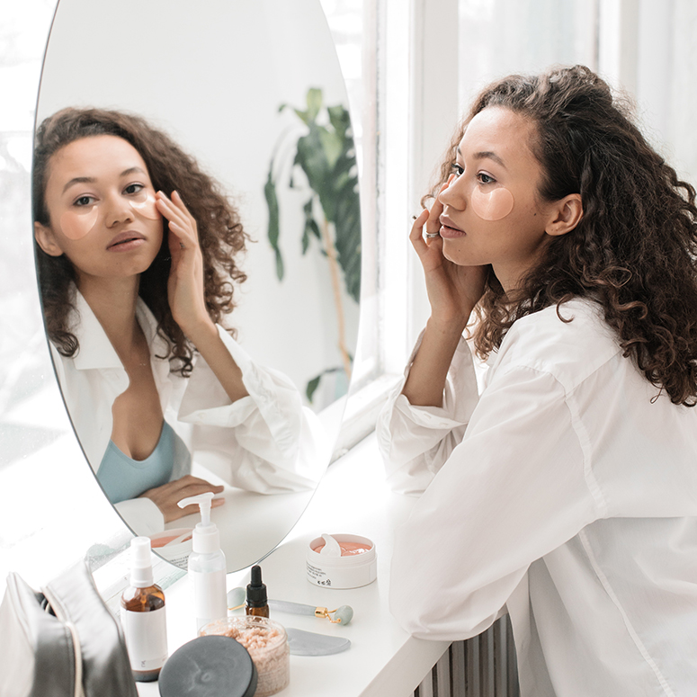 a young Black woman going through her skincare routine in front of a mirror