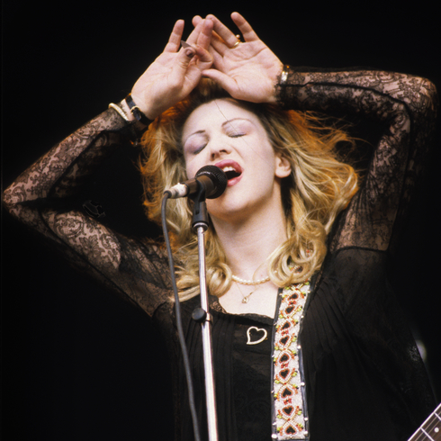 Courtney Love performing on stage as Hole with her eyes closed and hands above her head as she sings
