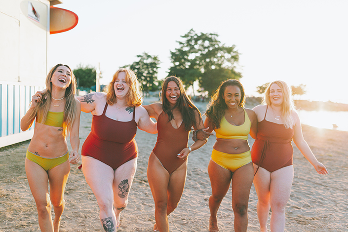a diverse group of girlfriends laughing together in bathing suits on the beach