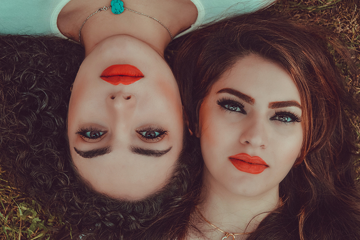 women with red lips laying with faces side to side 