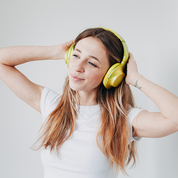 a young white woman with long hair wearing yellow headphones against a white background