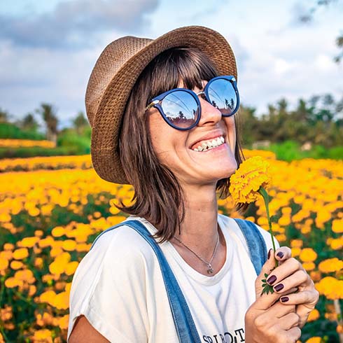 smiling young woman wearing a hat and sunglasses in field of flowers