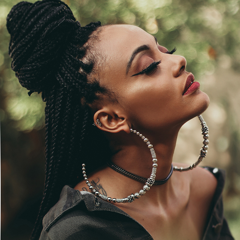 a young Black woman with large earrings looking up at the sky with eyes closed