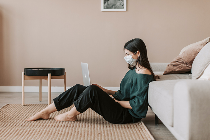 Woman with a mask sitting on the floor with her laptop