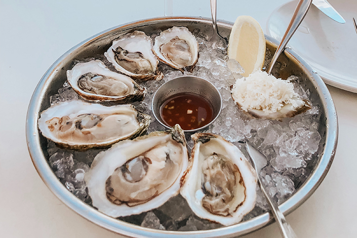 a platter of oysters on ice with sauce, sliced lemon and shredded horseradish