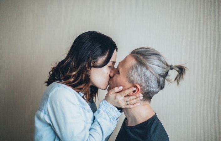 A man and woman kissing in front on a blank wall. 