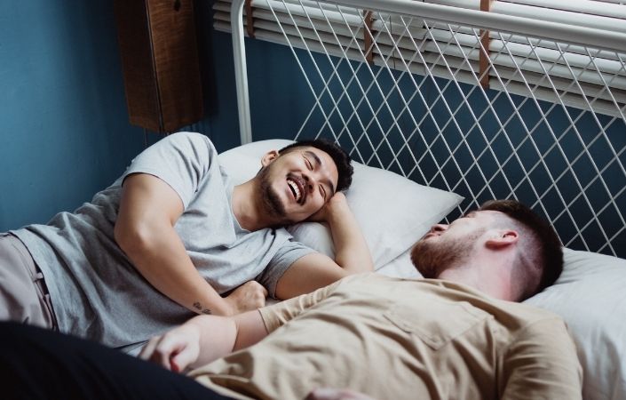 Two men romantically smiling and laughing in bed together. 