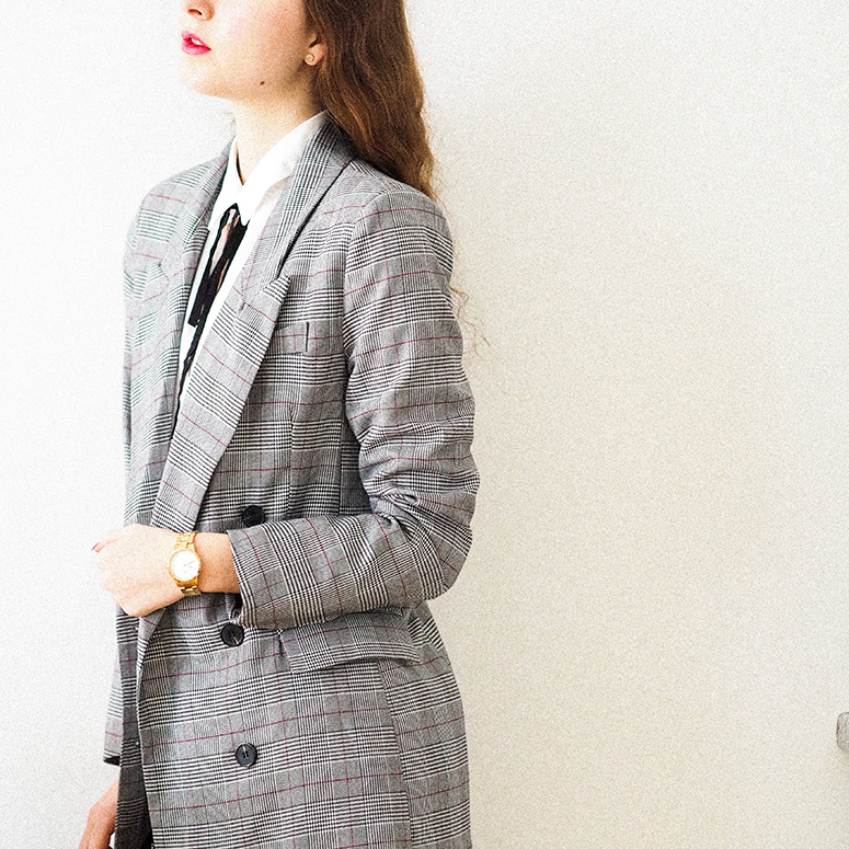 a young white woman standing to the side wearing an oversized grey blazer