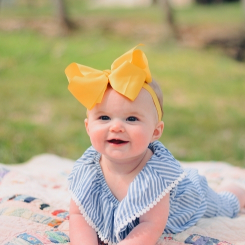Smiling baby wearing a blue dress and a yellow bow.