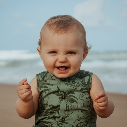 Baby wearing a green shirt on the beach.