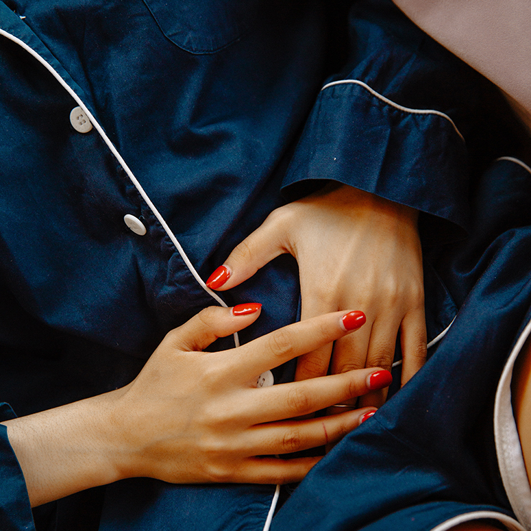 a white woman with red nails holding her stomach, wearing PJs