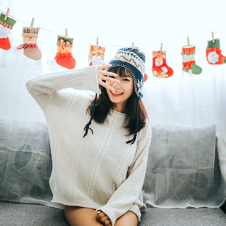 Woman sitting on couch in a sweater and winter toque with holiday stockings strung across behind her