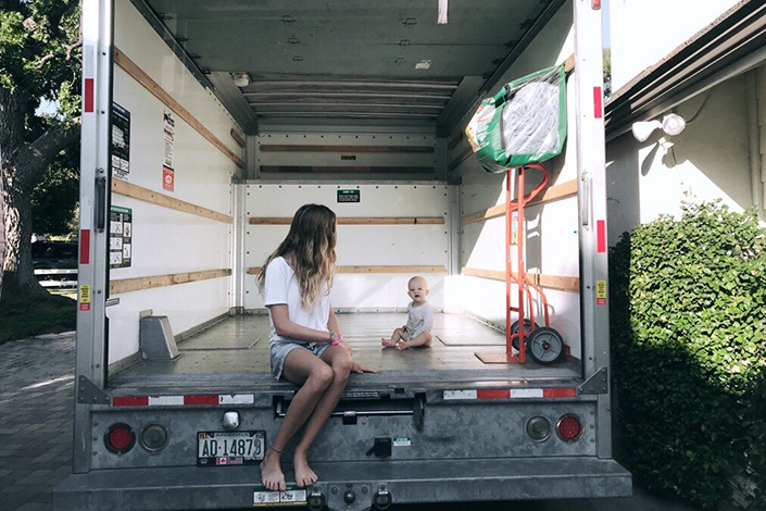 Woman in a moving truck with a small toddler sitting inside