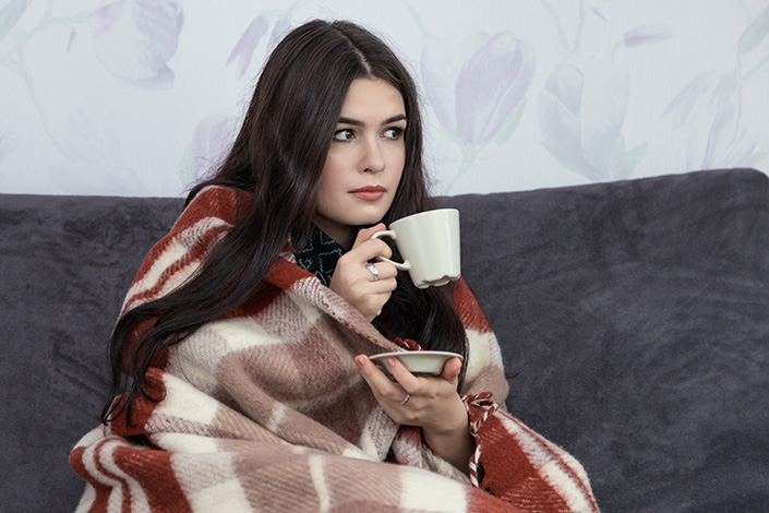 Woman on a couch, wrapped in a blanket with a warm cup of coffee