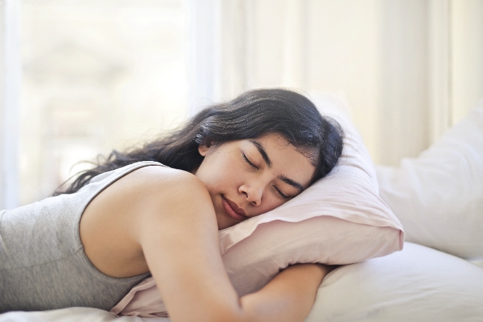 A woman sleeping on her stomach while hugging a pink pillow