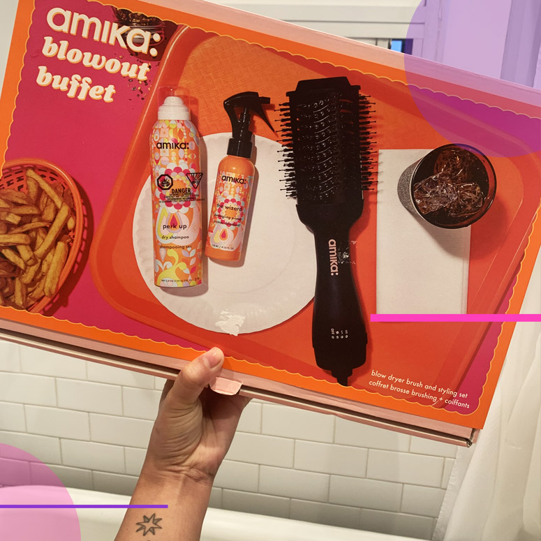 amika: blowout buffet product set being held up by a hand in a washroom