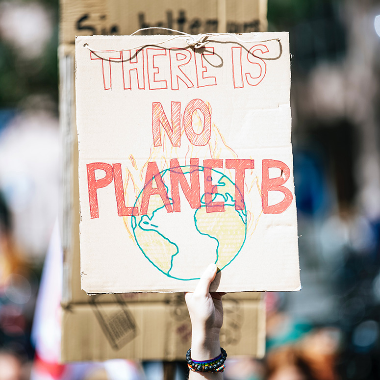 a woman's hand holding up a cardboard sign that reads 'There is No Planet B'