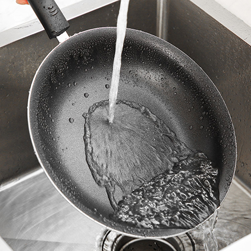 A non-stick pan being rinsed under running water over a sink.