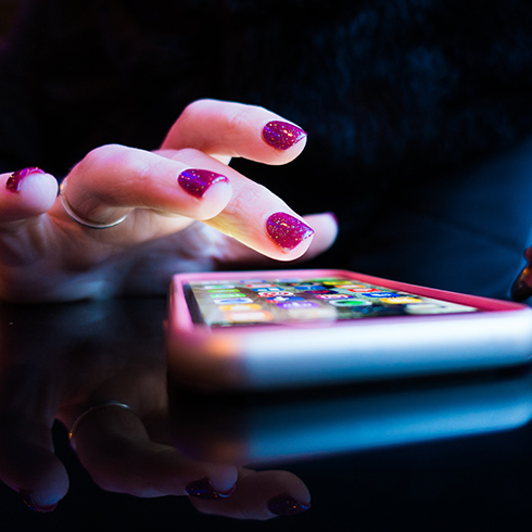 Close up of an iPhone sitting on a reflective black table and a hand with sparkly burgundy nails tapping the screen.