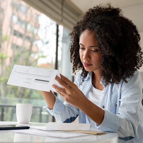 Attractive young mixed race woman sitting at a table looking at paper bills.