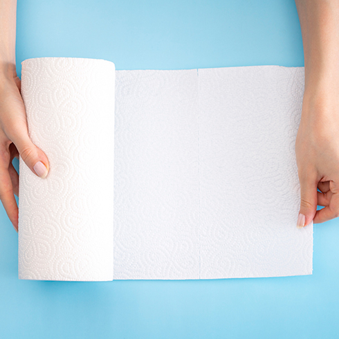 Birds-eye view of a woman using both hands to unroll paper towel on a light blue background.
