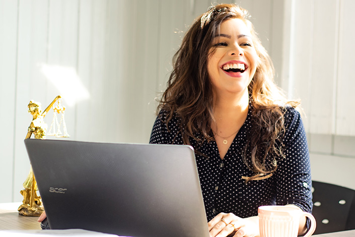 a young white woman laughing at work with an open laptop in front of her