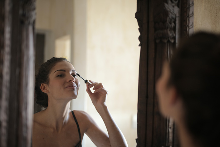 a young white woman applying makeup in the mirror