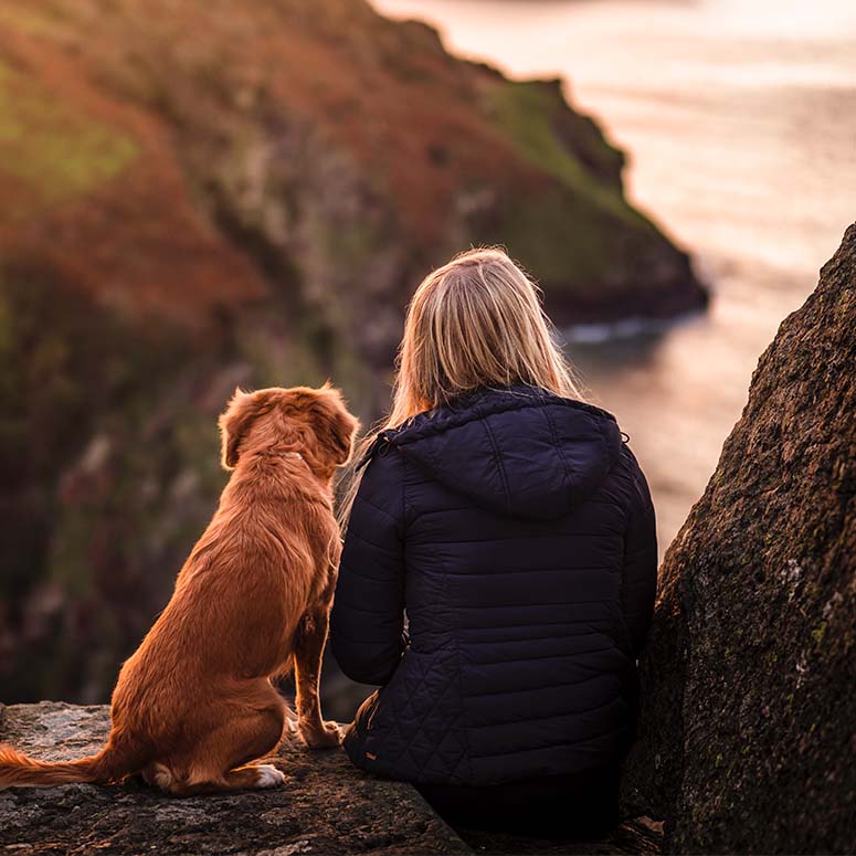 blonde woman and golden retriever sit on mountain