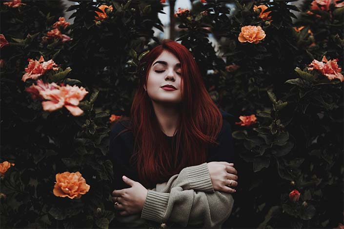 white woman with red hair stands with eyes closed in garden