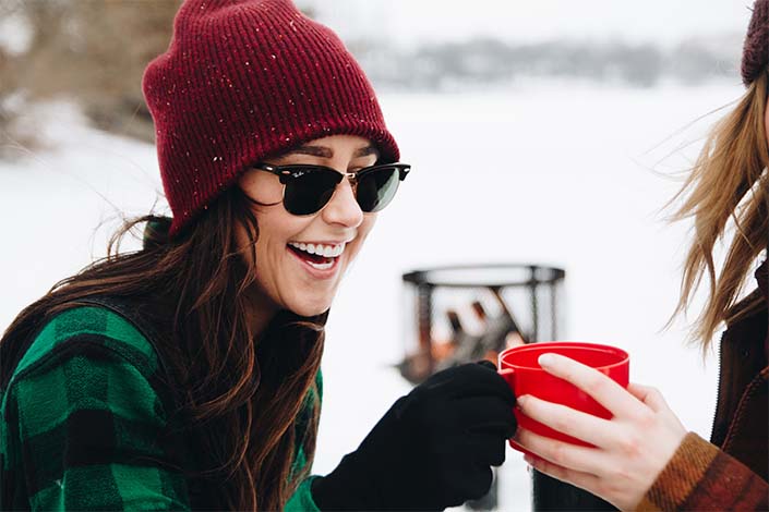 woman with long brown hair holding a red mug out in snowy landscape