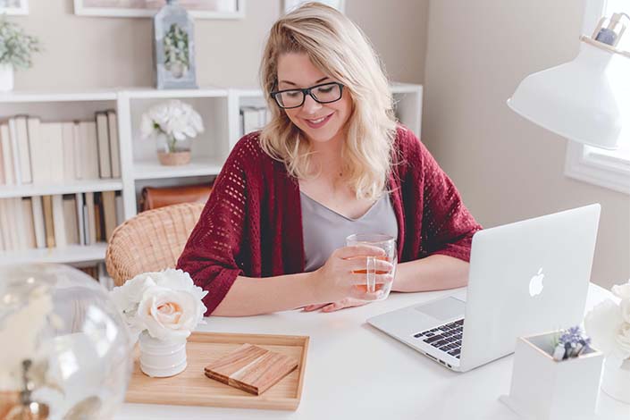 blonde woman wearing glasses smiles down at laptop