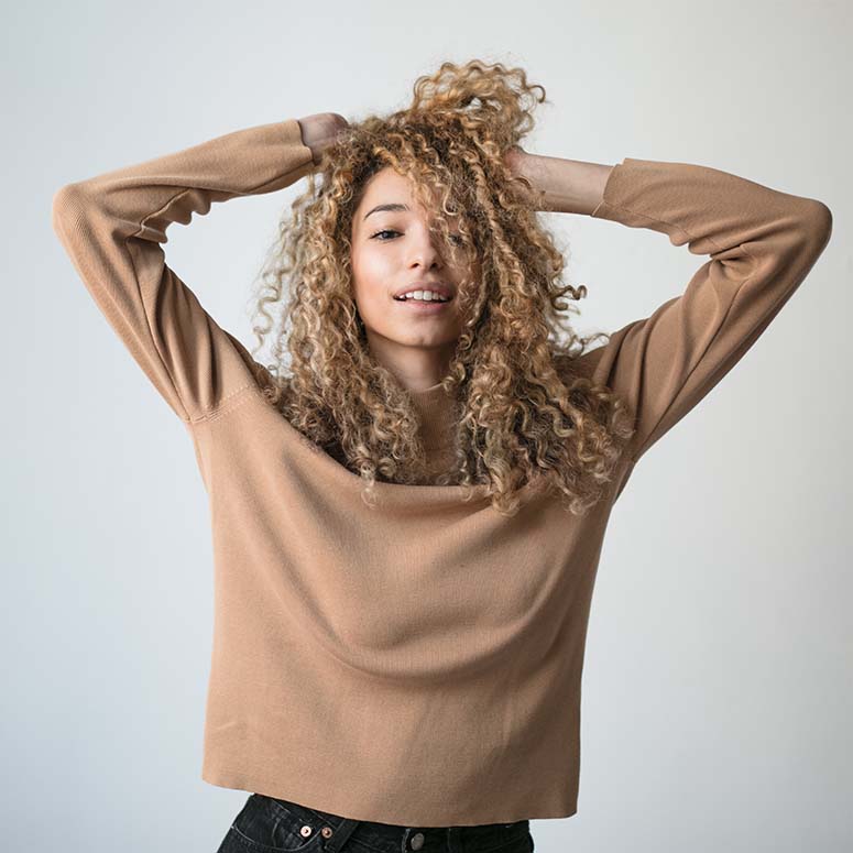 young woman with blonde curly hair raises her arms above her head