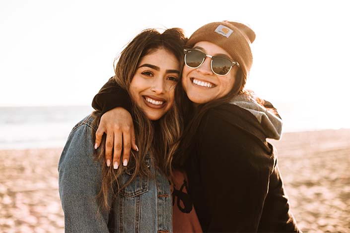 woman with brown hair hugging woman with hat and sunglasses