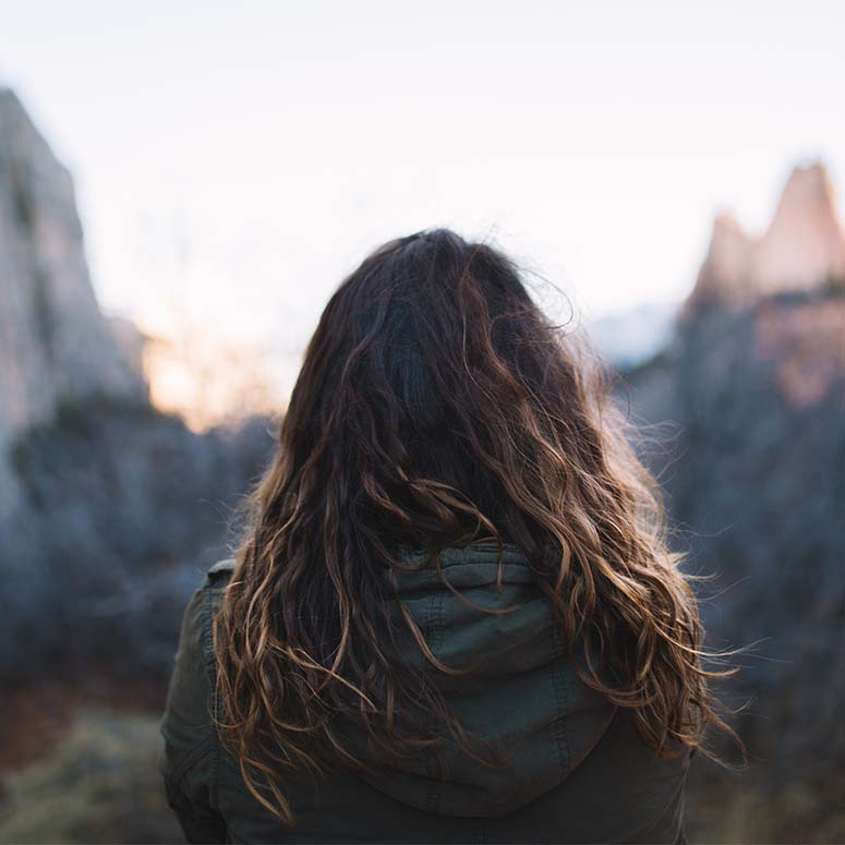 woman with wavy hair stands outside looking at mountains