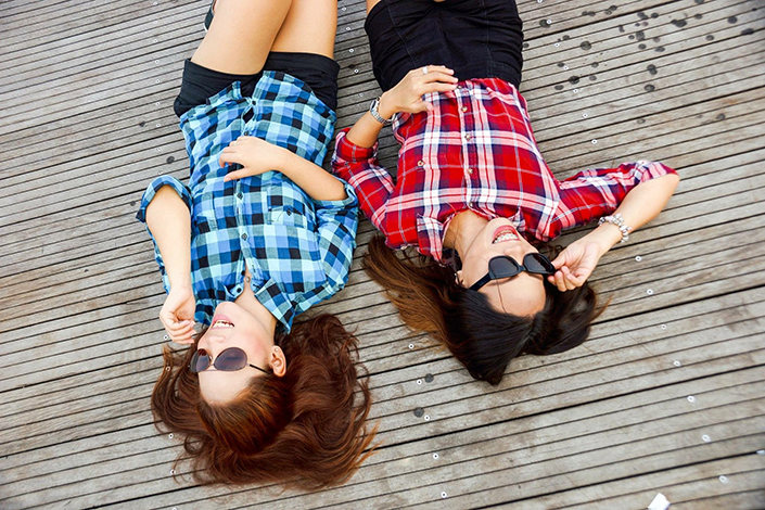 two young white women wearing sunglasses and lying on their backs outside
