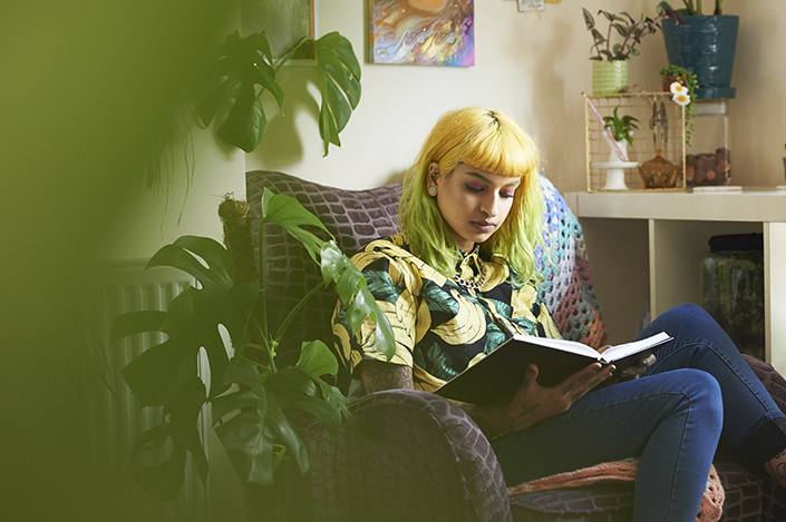 a young woman with bright yellow hair reading in her apartment and surrounded by plants