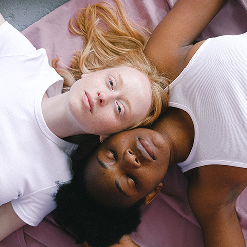 White woman and Black woman lying on pink mat