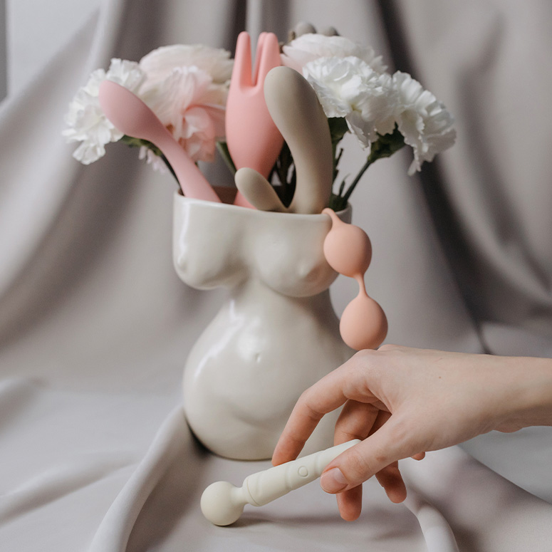 Flowers and sex toys in a female's body vase and a hand holding a sex toy in front