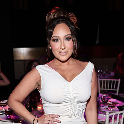 Adrienne Bailon wearing a white dress and hand on her hip
