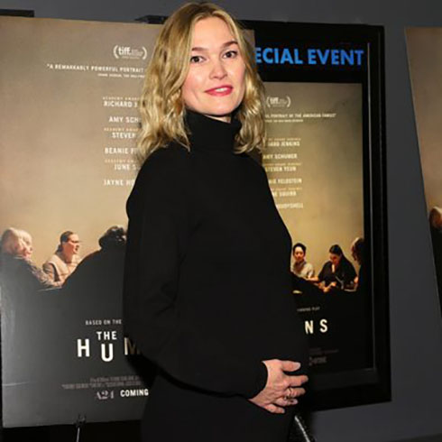 Julia Stiles wearing a black dress holding her baby bump