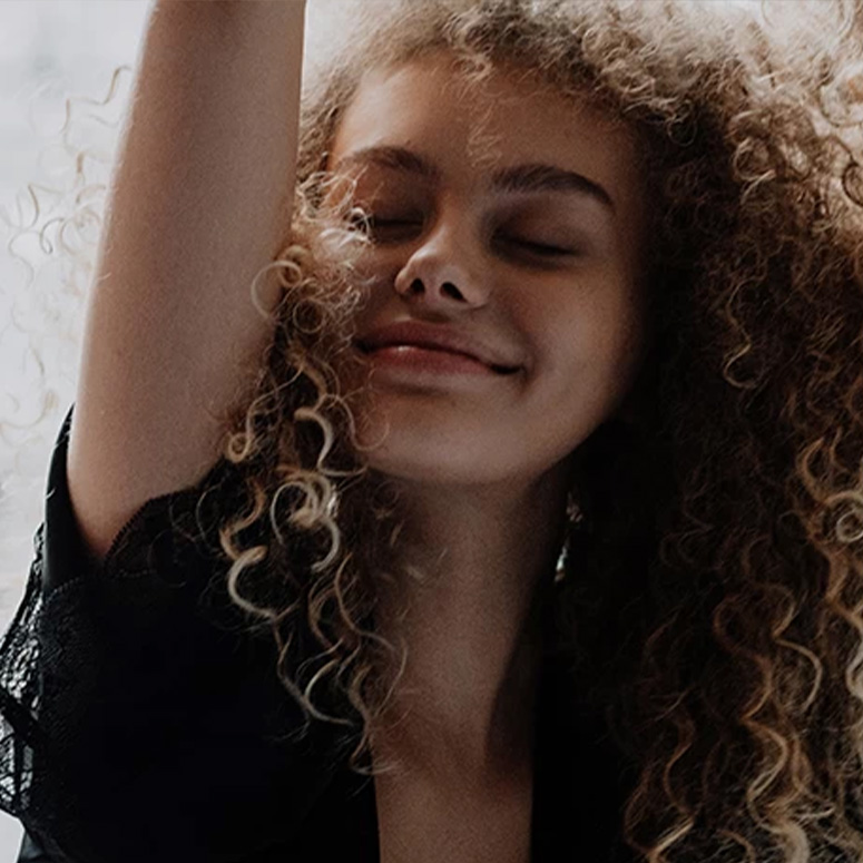 Young woman with curly hair smiling with her eyes closed and her arm in the air