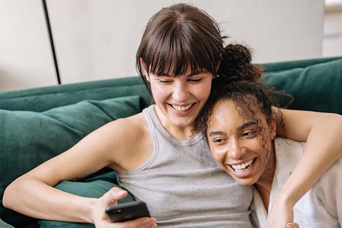 white woman and Black woman smiling and embracing on green couch