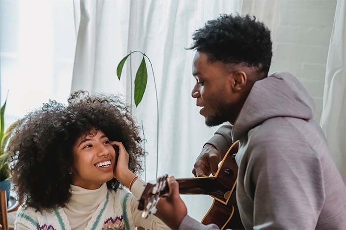 Black man plays guitar for smiling Black woman