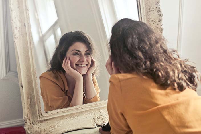 white woman with dark hair smiles while looking in mirror