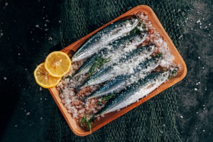 Square plate with four sardines, garnished with salt and orange wheels 