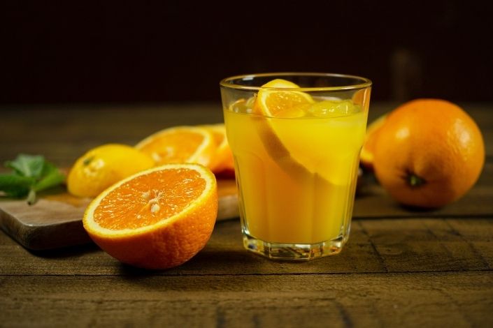 Glass of orange juice next to sliced oranges